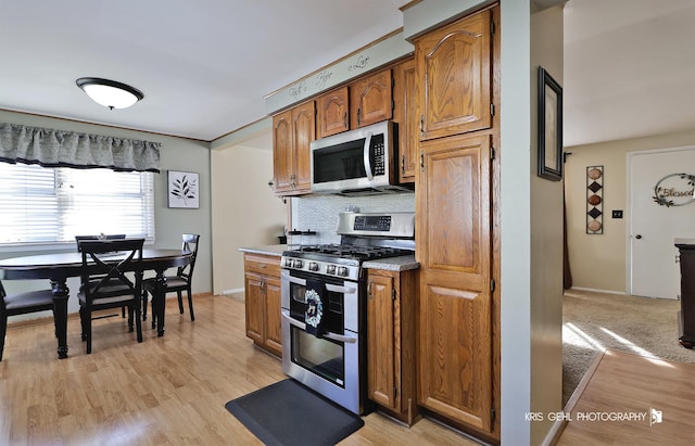 kitchen with tasteful backsplash, brown cabinets, stainless steel appliances, and light wood-style flooring