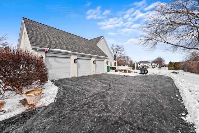 view of snow covered exterior featuring aphalt driveway, an attached garage, and brick siding