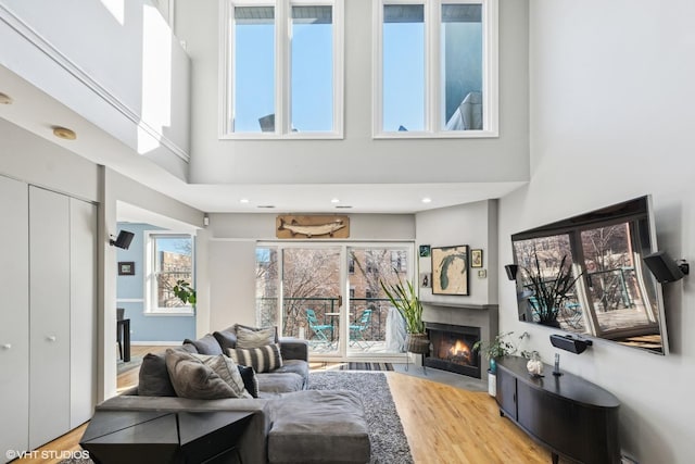 living room featuring a tile fireplace, a towering ceiling, and light wood-style floors