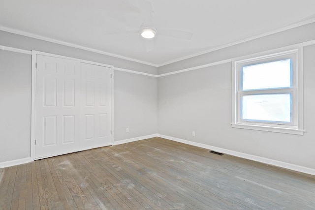 unfurnished bedroom featuring crown molding, wood-type flooring, visible vents, a ceiling fan, and baseboards