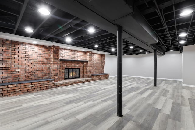 finished basement with brick wall, a fireplace, wood finished floors, and baseboards