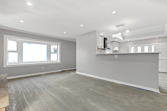 unfurnished living room featuring baseboards, a raised ceiling, wood finished floors, and recessed lighting