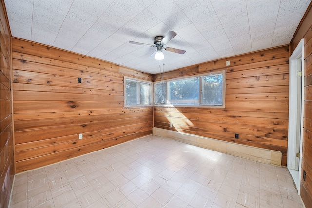 empty room featuring a ceiling fan, wood walls, and light floors