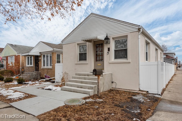 bungalow-style home featuring brick siding, fence, and stucco siding