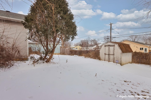 snowy yard featuring a storage shed, fence, and an outbuilding