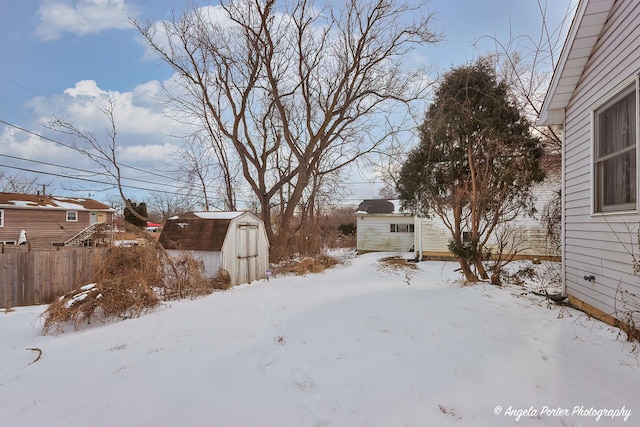 snowy yard featuring an outbuilding, fence, and a shed