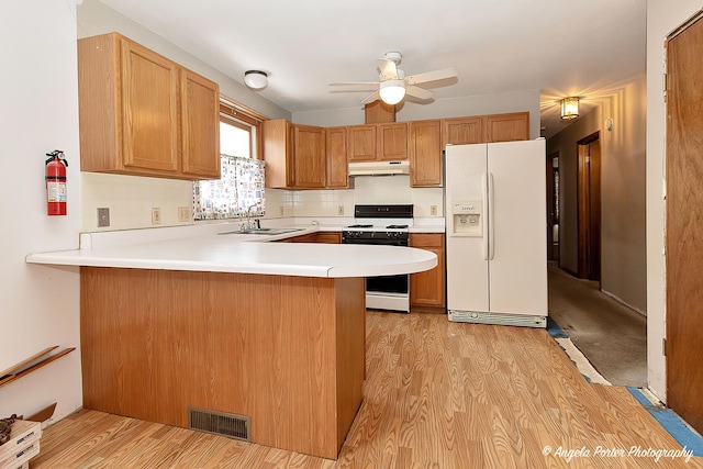 kitchen with white appliances, visible vents, a peninsula, light countertops, and under cabinet range hood