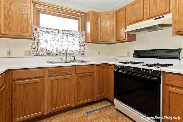 kitchen featuring tasteful backsplash, range with gas stovetop, light countertops, under cabinet range hood, and a sink