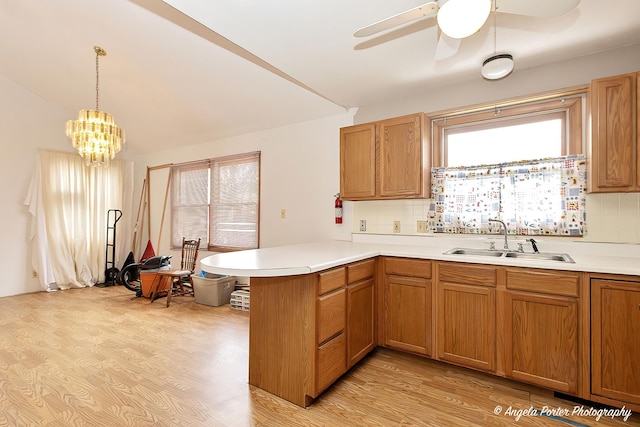 kitchen featuring pendant lighting, light countertops, light wood-style floors, a sink, and a peninsula