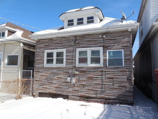 view of snow covered exterior with stone siding and fence