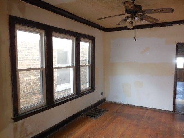 empty room featuring a ceiling fan, crown molding, visible vents, and dark wood-style flooring