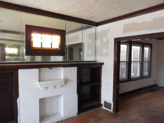 interior space with visible vents, ornamental molding, wood finished floors, a textured ceiling, and a brick fireplace