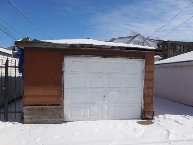 snow covered garage featuring a garage and fence