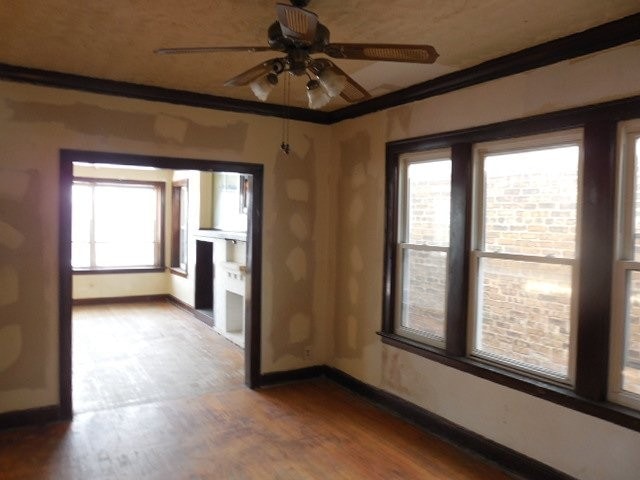 unfurnished room with ornamental molding, wood finished floors, a ceiling fan, and baseboards