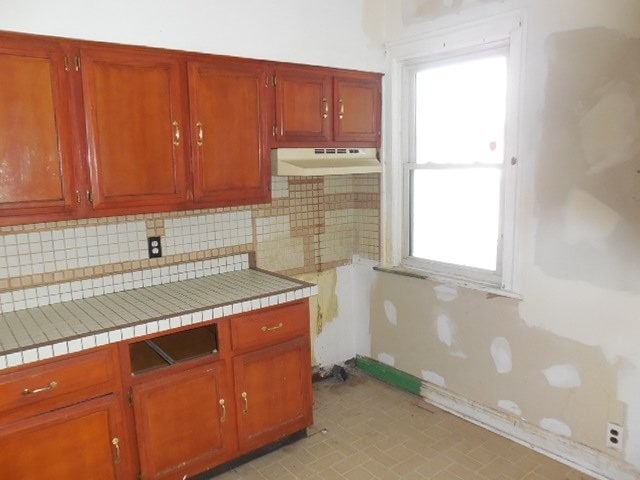 kitchen featuring tile countertops, baseboards, decorative backsplash, and under cabinet range hood