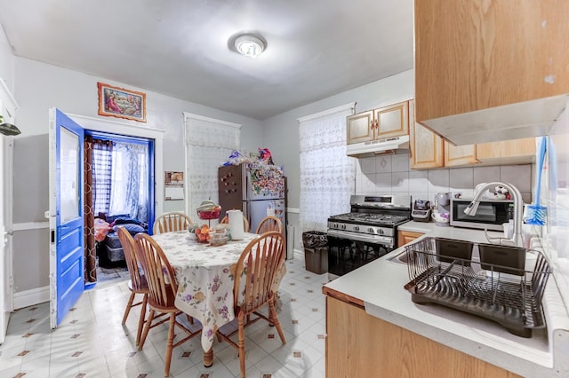 kitchen with under cabinet range hood, stainless steel appliances, light countertops, light floors, and tasteful backsplash