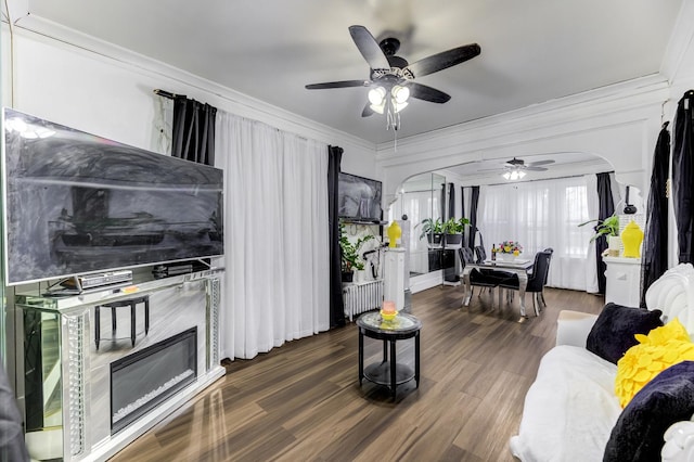 living area with arched walkways, crown molding, and wood finished floors