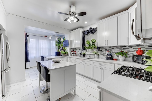 kitchen featuring white cabinets, decorative backsplash, ceiling fan, freestanding refrigerator, and a sink