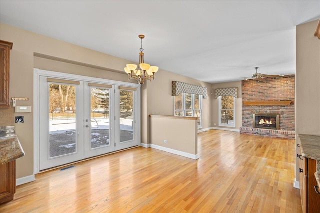 interior space featuring light wood finished floors, a fireplace, baseboards, and ceiling fan with notable chandelier