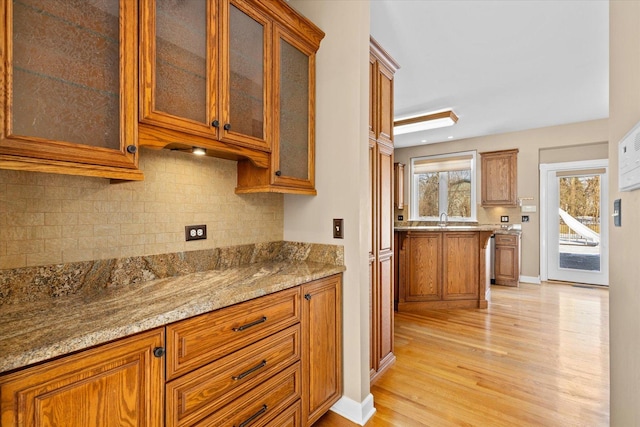 kitchen with light stone counters, light wood-style flooring, glass insert cabinets, and brown cabinets