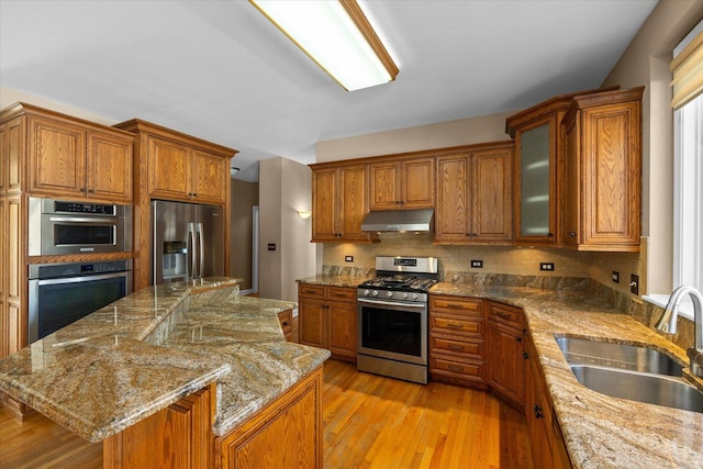 kitchen with under cabinet range hood, a kitchen island, a sink, appliances with stainless steel finishes, and glass insert cabinets