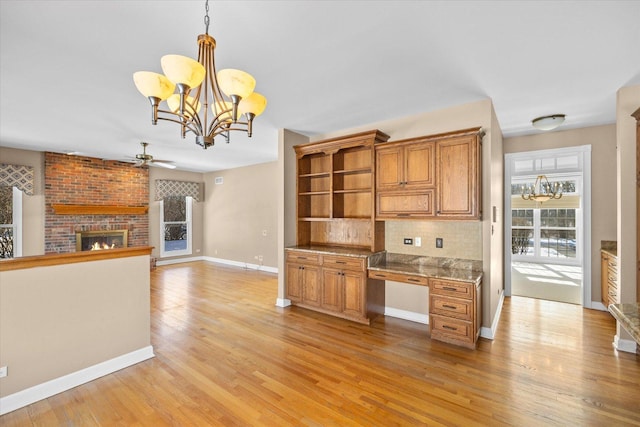 kitchen with decorative light fixtures, built in desk, tasteful backsplash, a brick fireplace, and light wood-type flooring