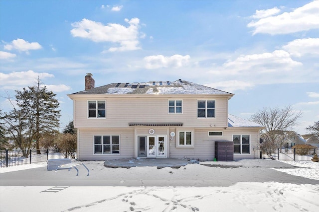 snow covered property with french doors, a chimney, and fence