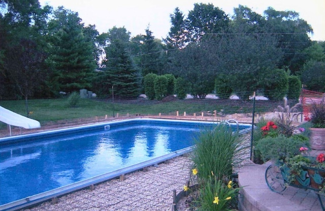 outdoor pool with a water slide and a lawn