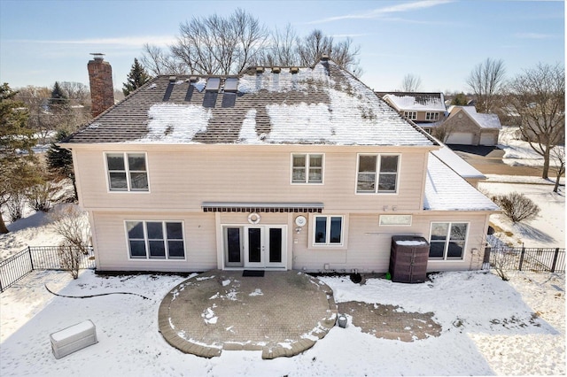 snow covered rear of property featuring french doors, fence, and a chimney