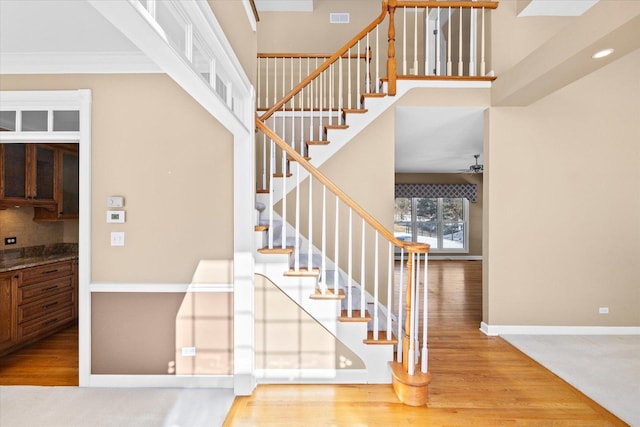 staircase with ceiling fan, wood finished floors, visible vents, and baseboards