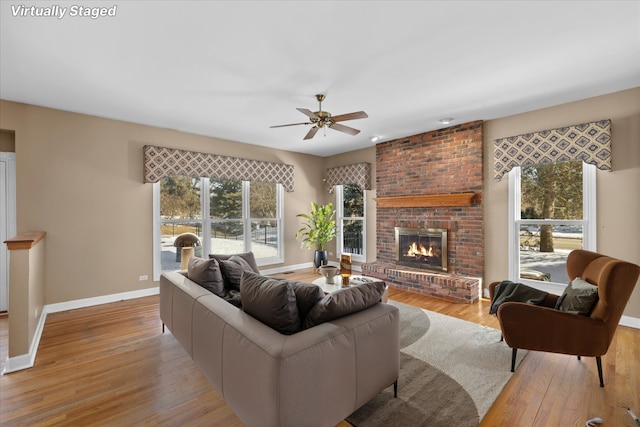 living room featuring a brick fireplace, light wood-style flooring, baseboards, and a ceiling fan