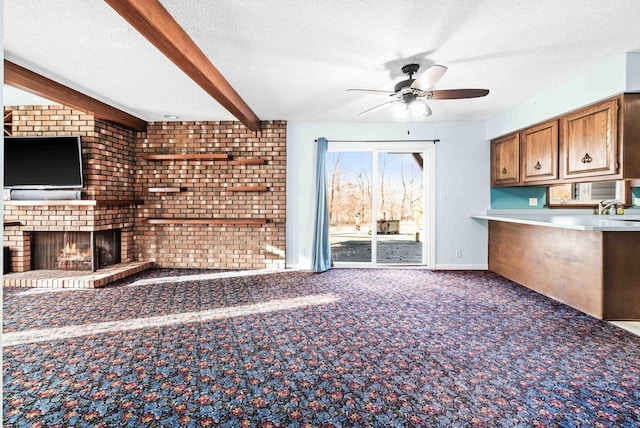 unfurnished living room featuring a textured ceiling, beam ceiling, a fireplace, and carpet flooring