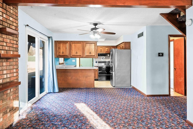 kitchen featuring visible vents, brown cabinetry, freestanding refrigerator, a textured ceiling, and range