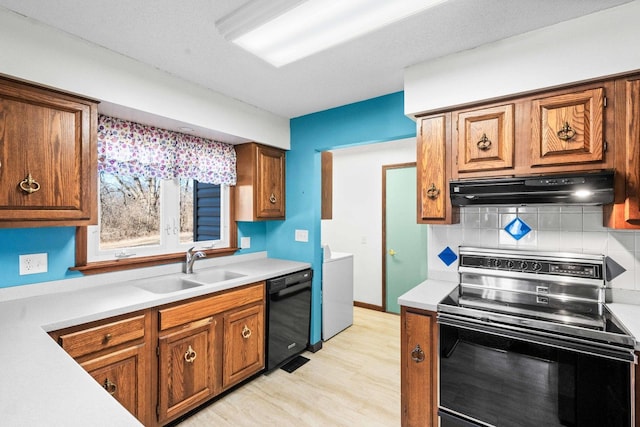 kitchen with under cabinet range hood, a sink, brown cabinets, black appliances, and tasteful backsplash