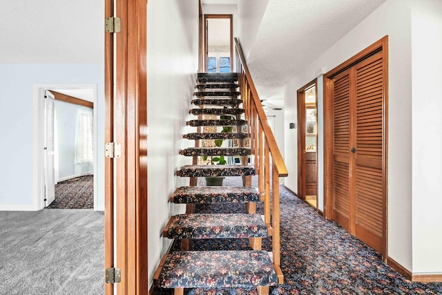 staircase with a textured ceiling, carpet flooring, and baseboards