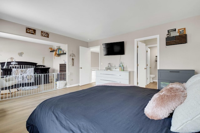 bedroom featuring baseboards, ensuite bath, and light wood-style floors