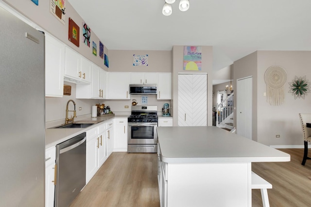 kitchen featuring appliances with stainless steel finishes, light countertops, a sink, and a center island