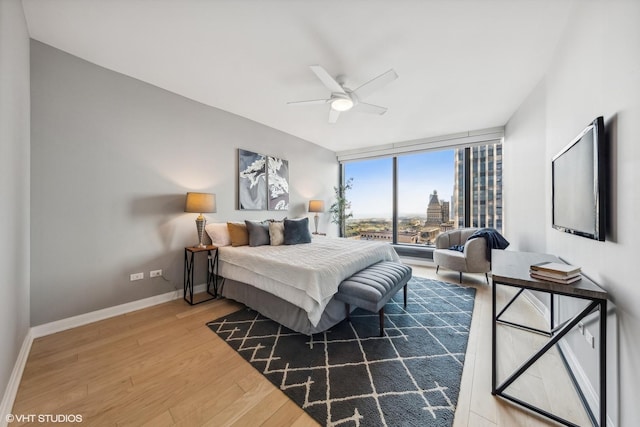 bedroom with expansive windows, ceiling fan, baseboards, and wood finished floors