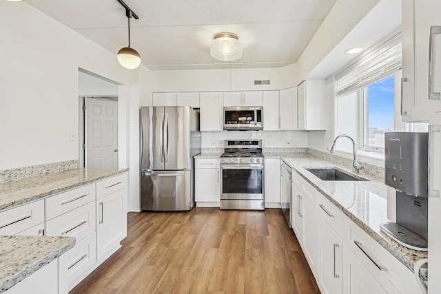 kitchen with hanging light fixtures, appliances with stainless steel finishes, white cabinets, and a sink