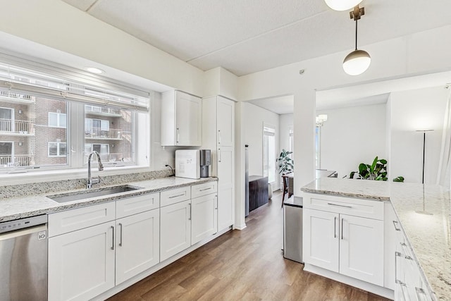 kitchen with white cabinets, dishwasher, light stone counters, hanging light fixtures, and a sink