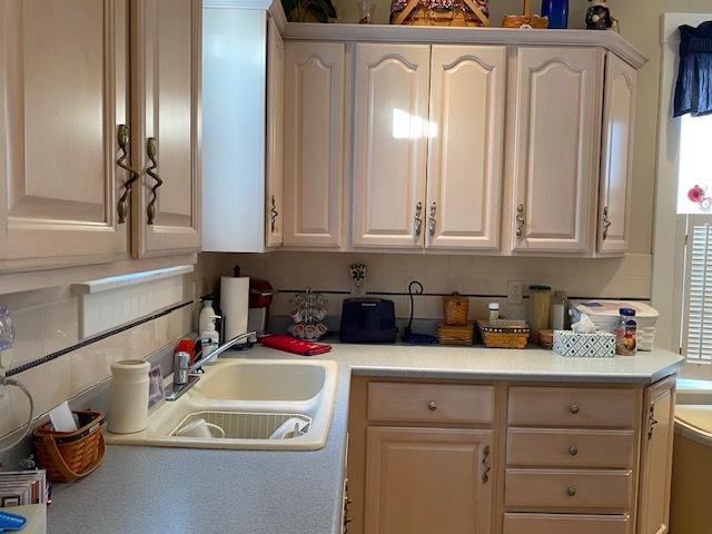 kitchen featuring white cabinets, light countertops, a sink, and backsplash