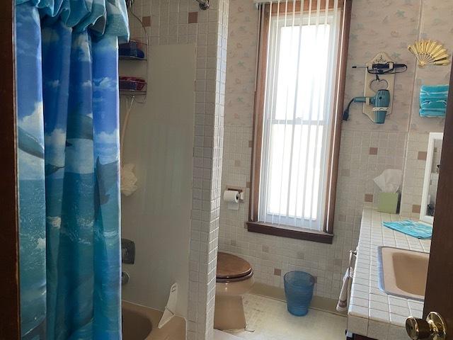 bathroom with shower / bathtub combination with curtain, tile walls, and wallpapered walls