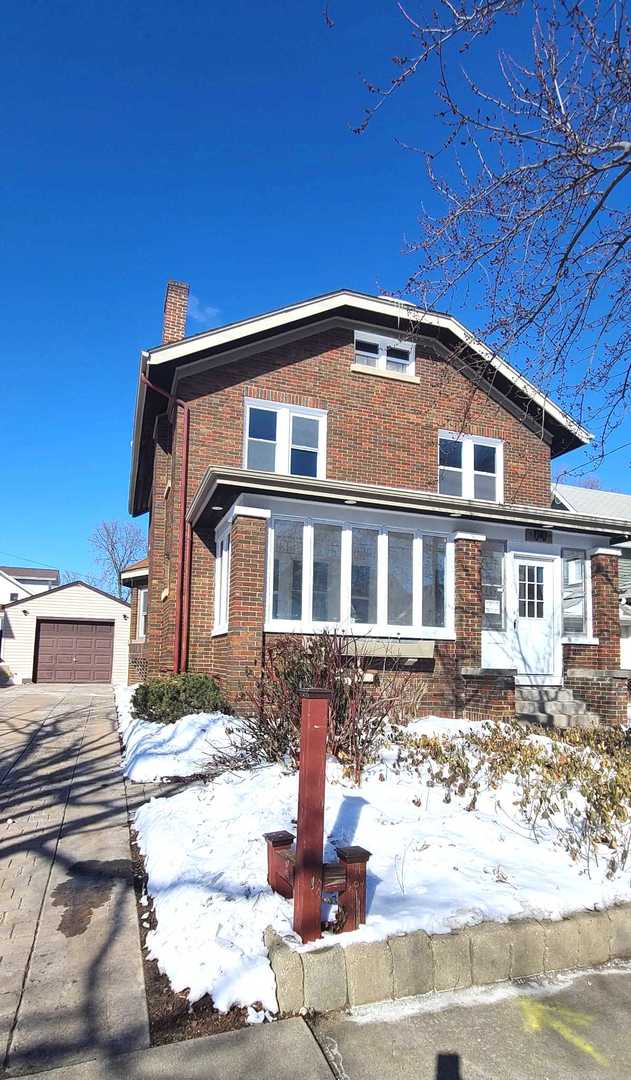 view of front of property with an outbuilding, brick siding, a chimney, and a garage