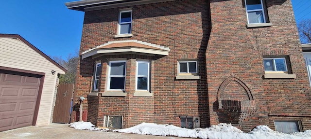 view of snowy exterior featuring a garage and brick siding