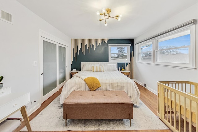 bedroom with an inviting chandelier, wood finished floors, visible vents, and baseboards