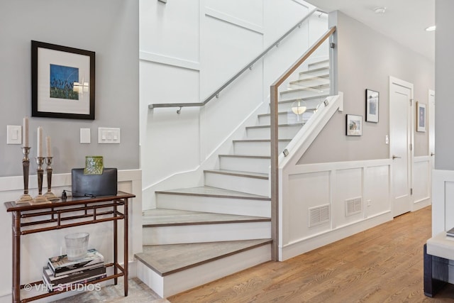 stairway with visible vents, wood finished floors, wainscoting, and a decorative wall