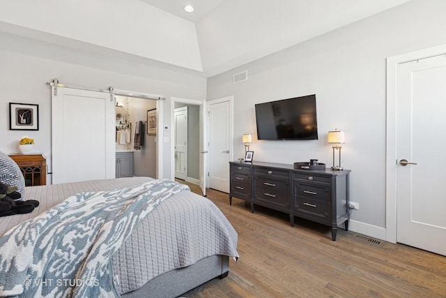 bedroom with visible vents, connected bathroom, baseboards, a barn door, and wood finished floors