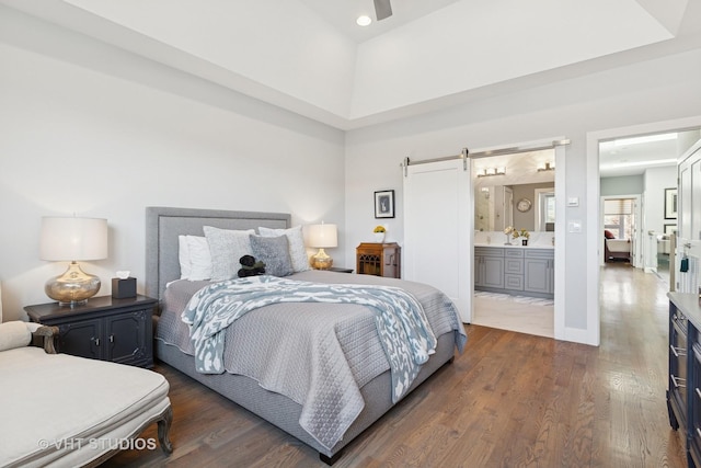 bedroom featuring a barn door, baseboards, ensuite bath, and wood finished floors