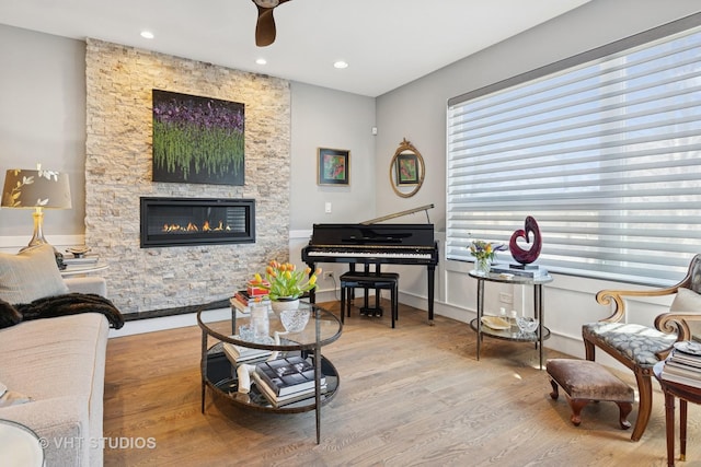 living area featuring recessed lighting, baseboards, a stone fireplace, and wood finished floors