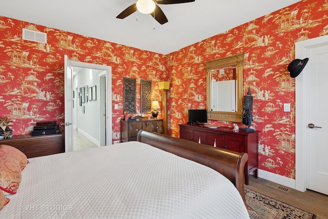 bedroom featuring visible vents, wood finished floors, wallpapered walls, baseboards, and ceiling fan